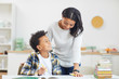 © Seventyfour - Portrait of cute African-American boy smiling at mother while studying at home in minimal white interior, copy space