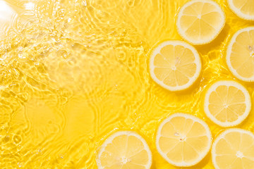 Wall Mural - Slice of lemon underwater or in water with splashing and droplet top view flat lay on yellow background