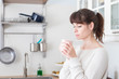 © silvia - Pretty caucasian woman, with bangs and ponytail, holding a cup of coffee in the morning in a white, bright lit, kitchen. Profile portrait. Relaxed and positive atmosphere.