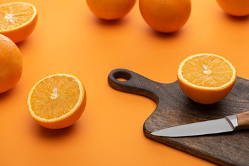 fresh juicy whole and cut oranges on cutting board with knife on colorful background