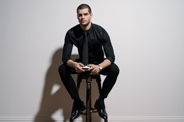 Young handsome businessman in black shirt and black suit. Confident young businessman posing on white background. Holding a game joystick