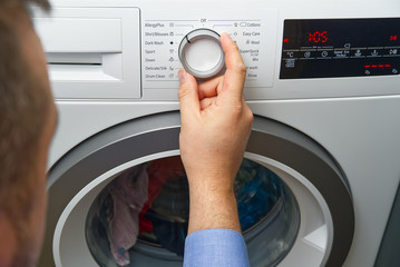 The man sets the program and turns on the washing machine. Close-up Of Person Hand Pressing Button Of Washing Machine For Clothes Laundry