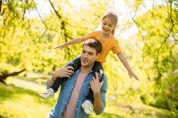 Wall Mural - Cute little girl sitting on father shoulders in the park