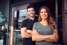 Portrait Of Couple Starting New Coffee Shop Or Restaurant Business Standing In Doorway