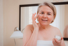 Smiling Senior Woman Applying Anti-aging Lotion To Remove Dark Circles Under Eyes.