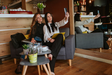 Two beautiful caucasian business women are sitting in a cafe, using a phone and a laptop. Work in a cafe