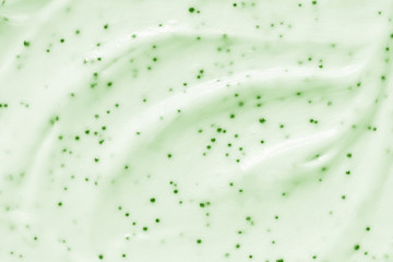 Face cream scrub texture background. Green color exfoliating skincare product smear smudge swatch. Gentle creamy scrub cleanser strokes closeup