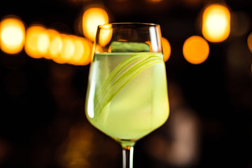 Wall Mural - A close-up of a beautiful light green cocktail with celery in a wine glass, bokeh lights, selective focus, horizontal