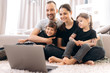 © Kateryna - Video call. Happy cheerful family. Young parents and their two amazing daughters communicate via video conference with grandparents sitting at home on the floor  in stylish casual wear