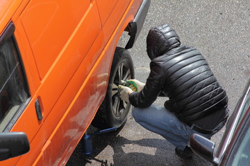 Wall Mural - A man in jeans and a hooded jacket removes the rear wheel of a yellow minibus, replacing a punctured car wheel in road conditions