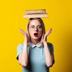 Wall Mural - Blonde girl in blue dress and glasses with books on yellow background