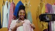 © Fractal Pictures - Joyful nice-looking fashion influencer young woman recording live streaming style vlog video talking on camera showing rack of stylish clothes isolated on background.