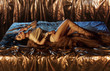 Passionate seductive sexy woman Queen Cleopatra art photo. fashion model beautiful body, long legs. girl lies at dark night on bed in royal golden room. ethnic costume dress. Gold Jewelry Accessories
