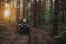 A Young Man In A White Helmet Rides Through The Woods On A Quad Bike. Extreme Hobby. A Trip To ATV On The Road From Logs. Quad Biking Through The Forest.