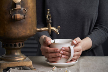 Wall Mural - Side view of female hands pouring cup of tea from vintage samovar and jar of homemade jam, tea party concept