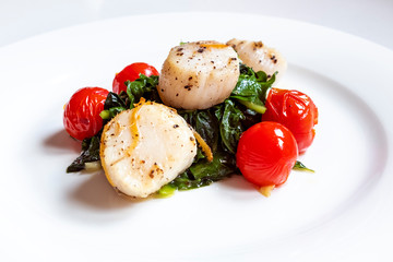 Pan Seared Scallops with Ginger and Black Pepper Served on a Bed of Green Swiss Chard and Decorated with Cooked Cherry Tomatoes