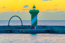 Catalonia, Spain. A Small Green And White Striped Lighthouse At The End Of The Breakwater Seawall Near Cruise Ship Port Of Barcelona.