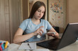 © byswat - Teenager girl, holding antiseptic spray in her hand, wipe to wipe off bacteria and viruses, homework on Internet, on laptop. Distance learning and training quarantine, stay at home. Virus protection.
