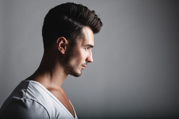 Male beauty concept. Portrait of handsome young man with stylish haircut posing over gray background. Perfect hair & skin. Close up. Studio shot