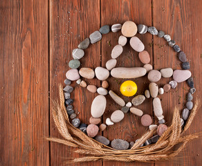 Pentagram made of stones with wheat ears and candle on a wooden background. Top view.