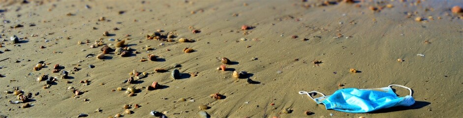 disposable face mask with small stones on the beach 