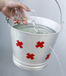 Hand pouring water from a glass into a leaking pail