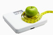 © ImageHit - Measuring tape wound around a green apple on a weighing scale