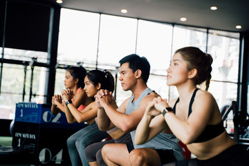 Group of athletic young Asian people in sportswear doing squat and exercising at the gym. Intense workout and healthy lifestyle concept