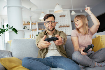 Wall Mural - Husband and wife playing video game with joysticks in living room.
Loving couple are playing video games at home.