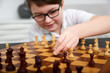 Small intelligent boy play chess and looks very clever and strategic, boy makes a move 