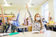 © Syda Productions - education, pandemic and health concept - group of students wearing face protective medical mask for protection from virus disease raising hands at school