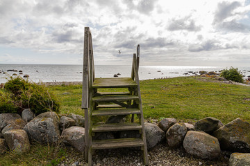  A beautiful view on the sea with wooden ladder, harsh stones, green grass and windy clouds