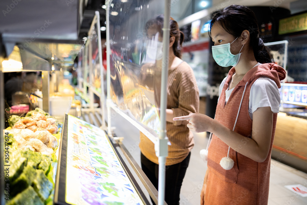 Asian child girl in a protective mask,ordering food in food court at the department store after Coronavirus quarantine Covid-19 with plastic shield partition,social distancing safety,new normal life - obrazy, fototapety, plakaty 