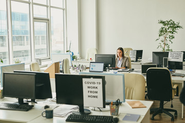 Wall Mural - One serious woman sitting in empty office during coronavirus quarantine and preparing report on computer