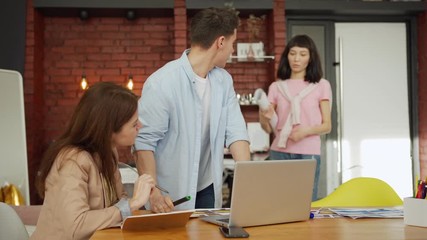Wall Mural - Creative young man and woman discussing business ideas at desk in office, female Asian colleague joining their conversation