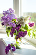 Vertical picture of bouquet of white, purple and violet lilac in glass jar on window sill with one branch laying down. Spring lilac floral blossom background. Aroma. Allergy