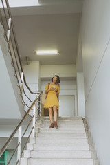 Wall Mural - Young Asian woman going down stairs and texting on her phone.