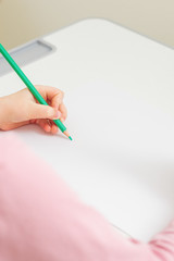 Wall Mural - Vertical image of little girl's left hand painting on the white paper with green pencil. Empty place. Mockup.