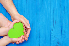 Top View Of Male And Child Hands Holding Paper Green Heart On Wooden Blue Background. Concept Of Family And Earth Day. Copy Space.