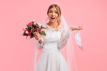 bride in a wedding dress with a medical protective mask in her hands, on a pink background. Quarantine, wedding, coronavirus