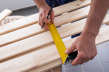 Carpenter measuring distance with construction ruler and drawing marks with pencil on wooden shelf. Senior man working at balcony. House improving and home decoration during quarantine concept