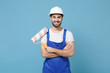© ViDi Studio - Smiling man in coveralls protective helmet hardhat hold paint roller isolated on blue background. Instruments accessories for renovation apartment room. Repair home concept. Holding hands crossed.
