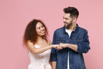 Wall Mural - Smiling couple friends european guy african american girl in casual clothes isolated on pastel pink background. People lifestyle concept. Mock up copy space. Giving fist bump, looking at each other.