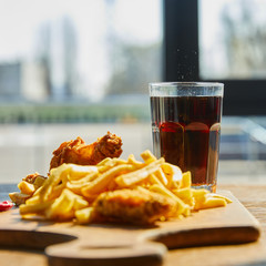 Wall Mural - selective focus of deep fried chicken, french fries on board with soda in glass on wooden table in sunlight near window