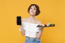 Young Woman Girl In Casual Clothes Hold In Hand Makizushi Sushi Roll Served On Black Plate Japanese Food Using Mobile Cell Phone Isolated On Yellow Background Studio Portrait. People Lifestyle Concept