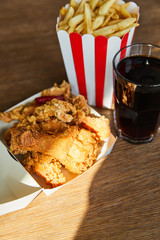 Wall Mural - selective focus of deep fried chicken, french fries and soda in glass on wooden table in sunlight
