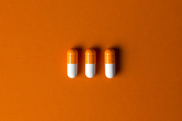 Wall Mural - The concept of positive. Three orange capsules on an orange background. Capsules lie in a row in the middle of the frame.