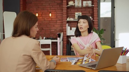 Wall Mural - Two young women discussing application interface templates sitting at desk in office, male colleague joining their discussion and explaining his ideas