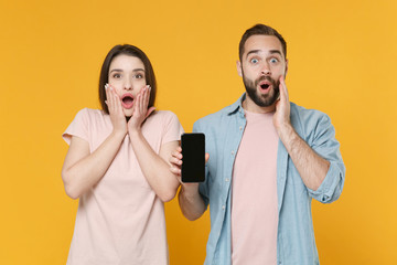 Wall Mural - Shocked young couple two friends guy girl in casual clothes isolated on yellow background. People lifestyle concept. Mock up copy space. Hold mobile phone with blank empty screen, put hands on cheeks.