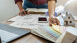 © PIC SNIPE - Interior designer choosing color in color swatch samples chart for house coloring selection in office with blueprint. Construction concept.